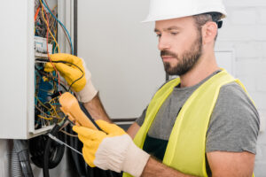 Professional electrician checking electrical panel with multimetr in corridor