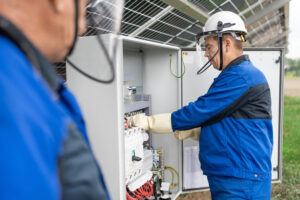 Two Service Engineers or electrician working on checking transformer site and solving problem for green energy solar power plant operation. Technician maintenance solar cells on Solar Energy Plant.