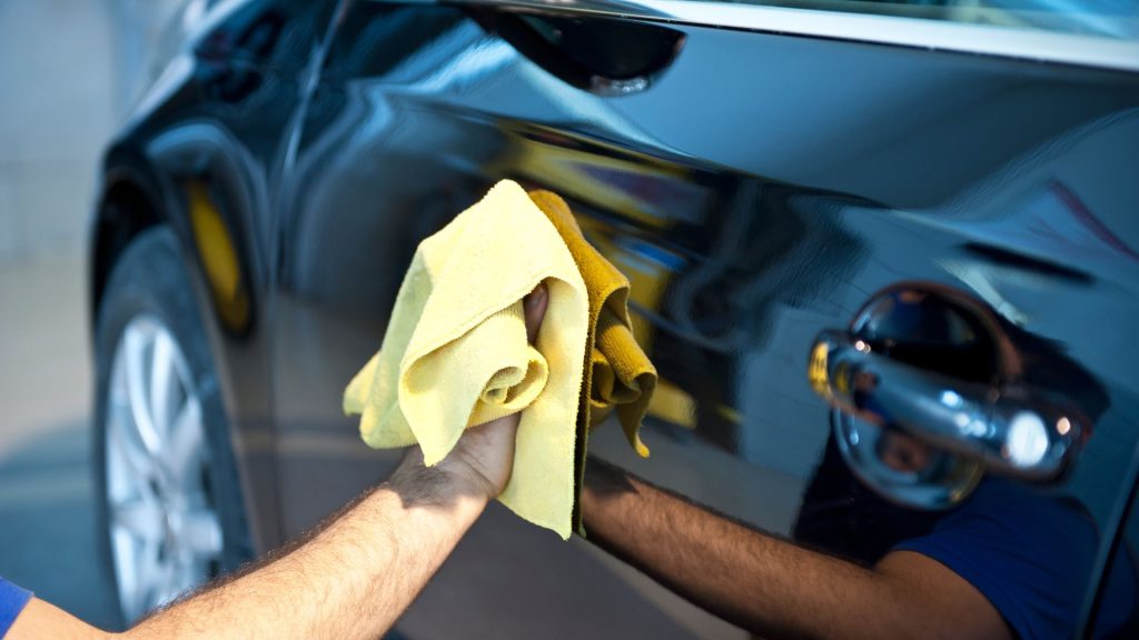 A worker wiping the side of a car