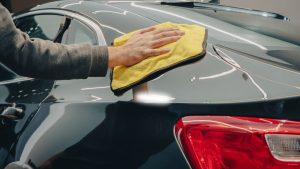 A worker holding an absorbent cloth to wipe the side of a car